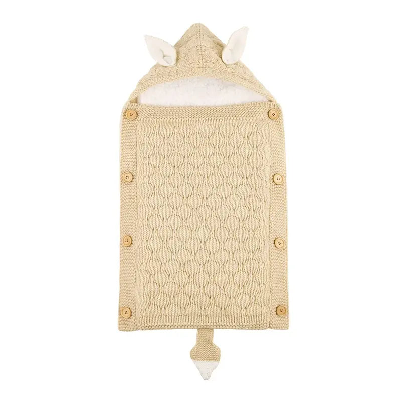 Nid d’ange bébé tricot beige avec capuche à oreilles, boutons en bois et maille texturée, présenté à plat sur fond clair.