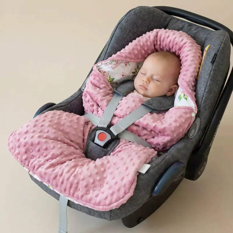 Bébé endormi installé dans un siège auto cosy avec une couverture nid d’ange polaire rose à reliefs et intérieur floral, harnais bien en place, ambiance douce et sécurisante.