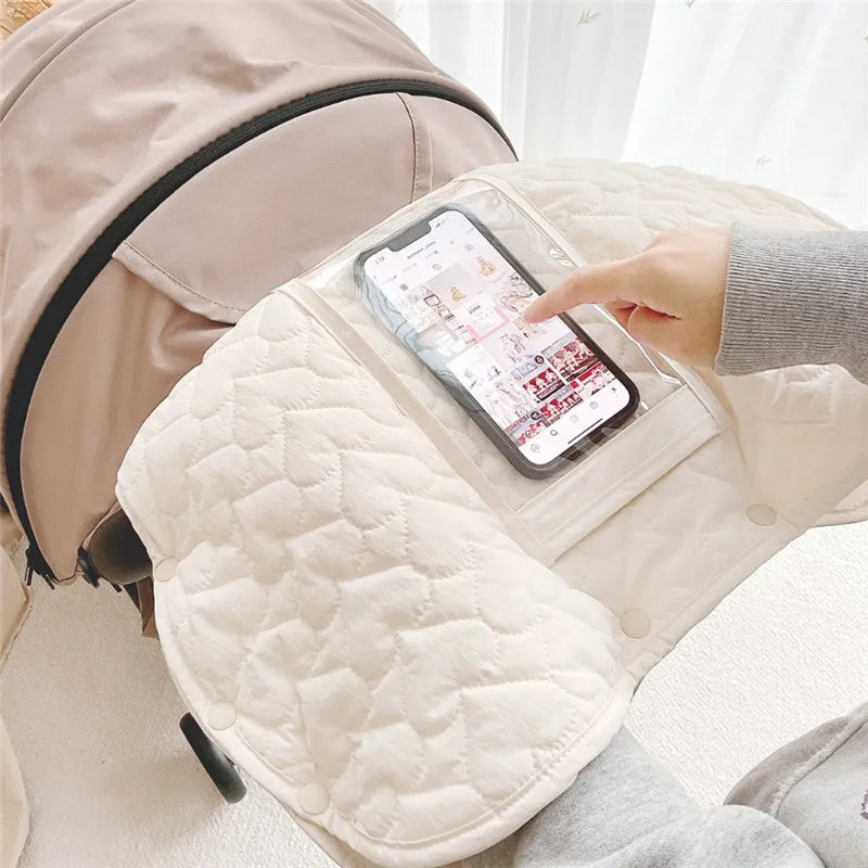 Manchon de poussette hiver avec poche transparente pour smartphone fixé sur la poignée, protégeant les mains du froid pendant la promenade